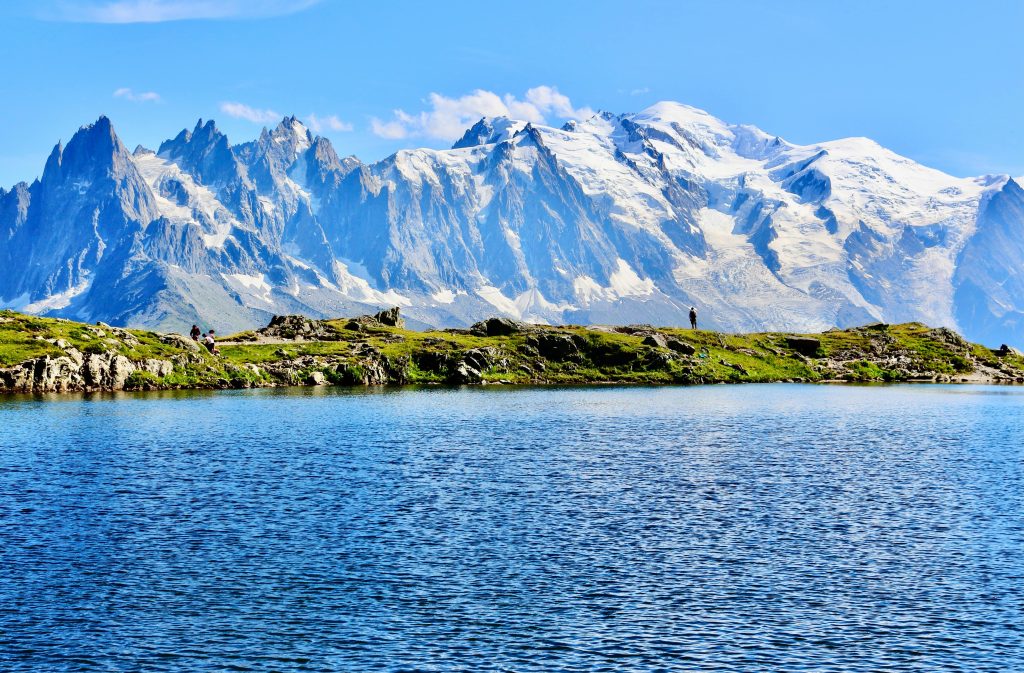 Breathtaking view of Mont Blanc's snowy peaks reflected in a pristine lake under a bright blue sky.