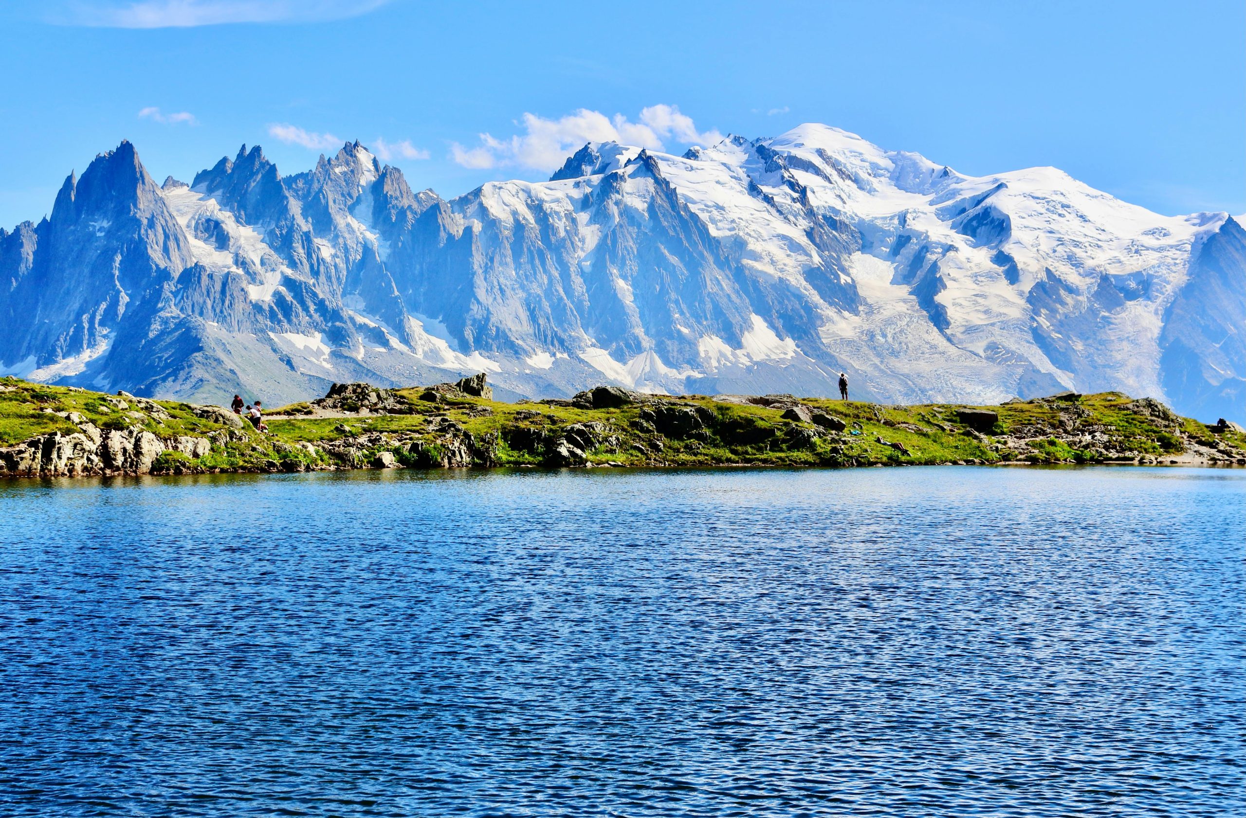 Breathtaking view of Mont Blanc's snowy peaks reflected in a pristine lake under a bright blue sky.
