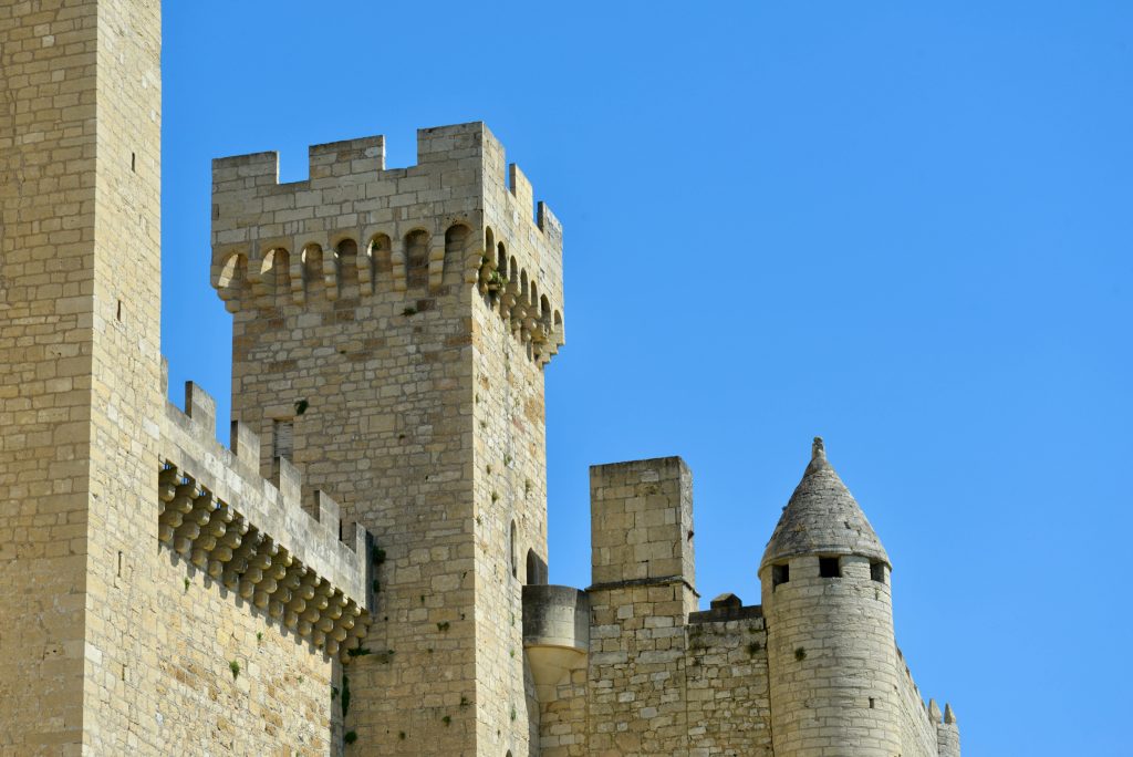 Low-angle view of Beynac Castle's stone turrets against a clear blue sky in France.