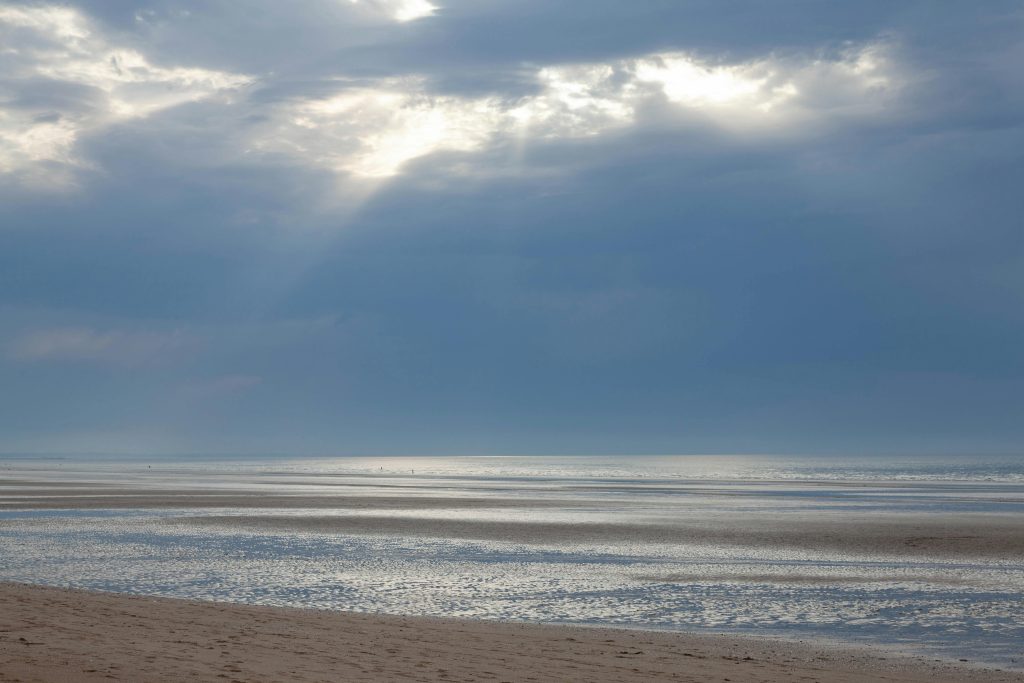 Peaceful seascape with sunbeams piercing clouds at Cabourg Beach, France.