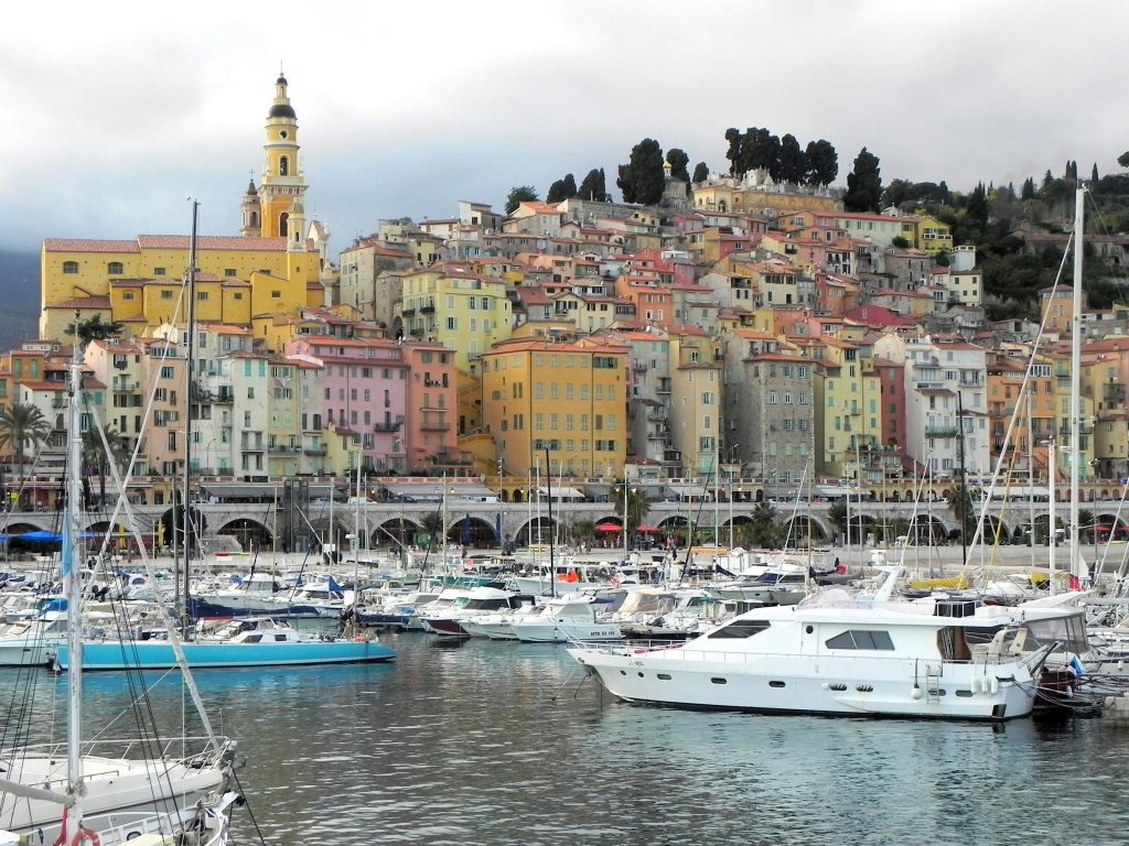 Colorful buildings overlook a lively harbor in Menton, France with yachts docked.