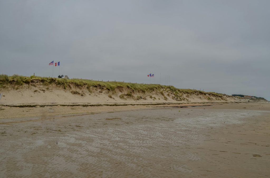 A historic view of Utah Beach in Normandy, France, with American and French flags symbolizing liberation.