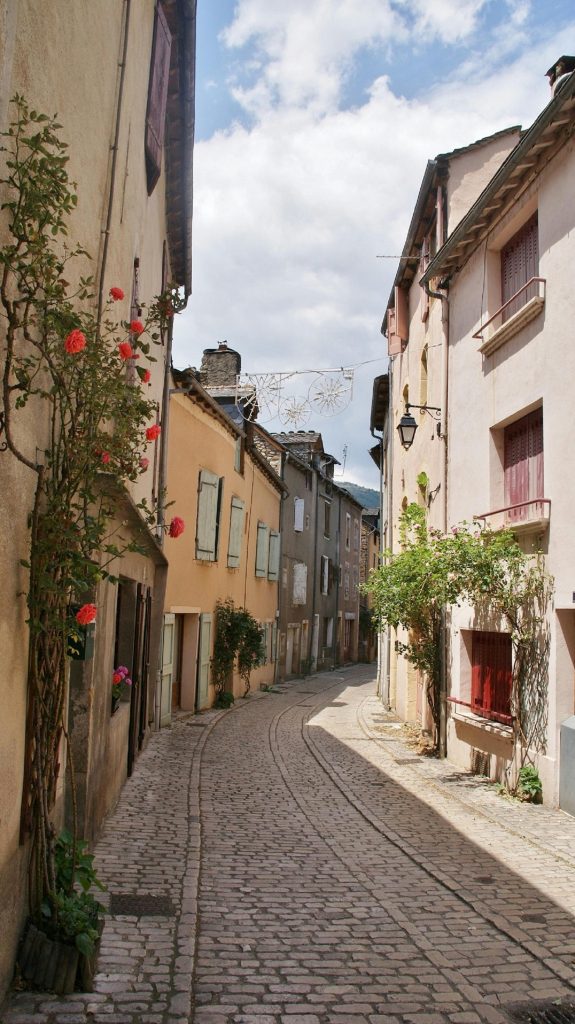Idyllic cobblestone street in Ispagnac, France with charming houses under a blue sky.