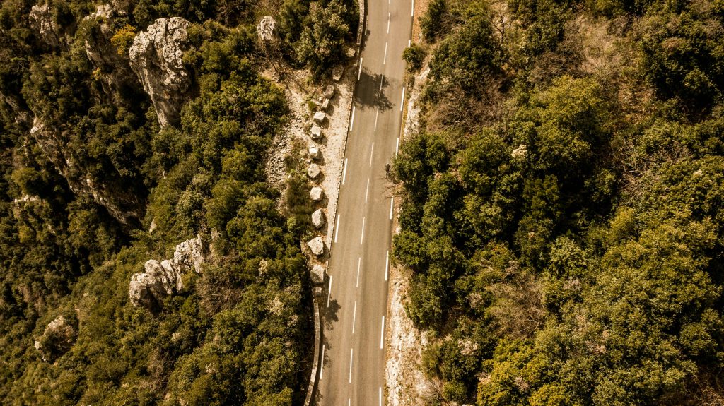 Aerial shot of a winding road through lush vegetation in a French forest.