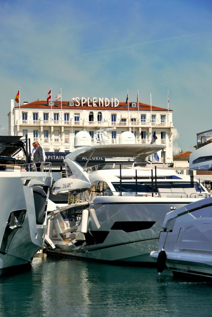Explore luxury yachts in Cannes marina with a backdrop of the iconic Splendid Hotel.