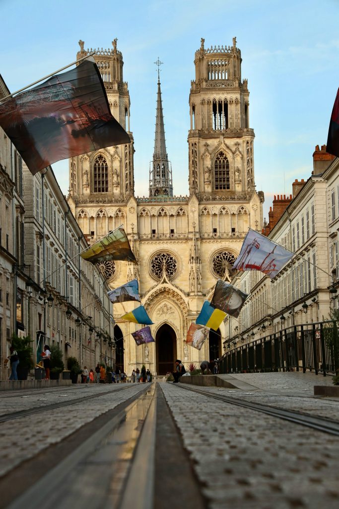 Orléans Cathedral under a blue sky with colorful flags lining the street.