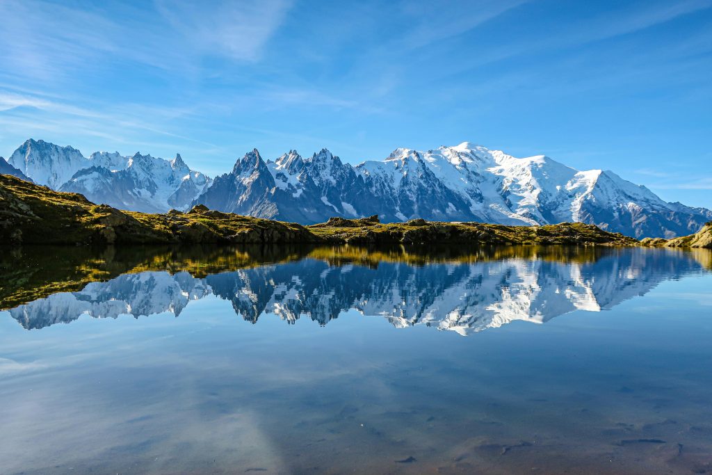 Beautiful reflection of Mont Blanc in a serene lake in Chamonix, France under a clear blue sky.
