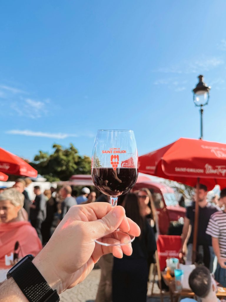 Hand holding wine glass at lively outdoor wine festival in Saint-Émilion.