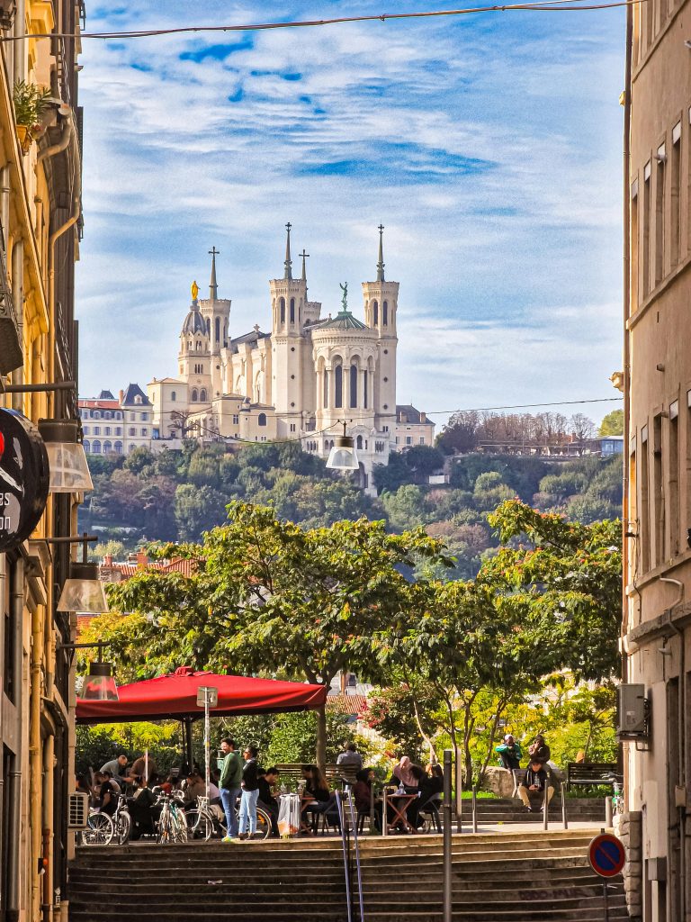 Vibrant street view of Lyon with the Basilica of Notre-Dame de Fourvière in the background.