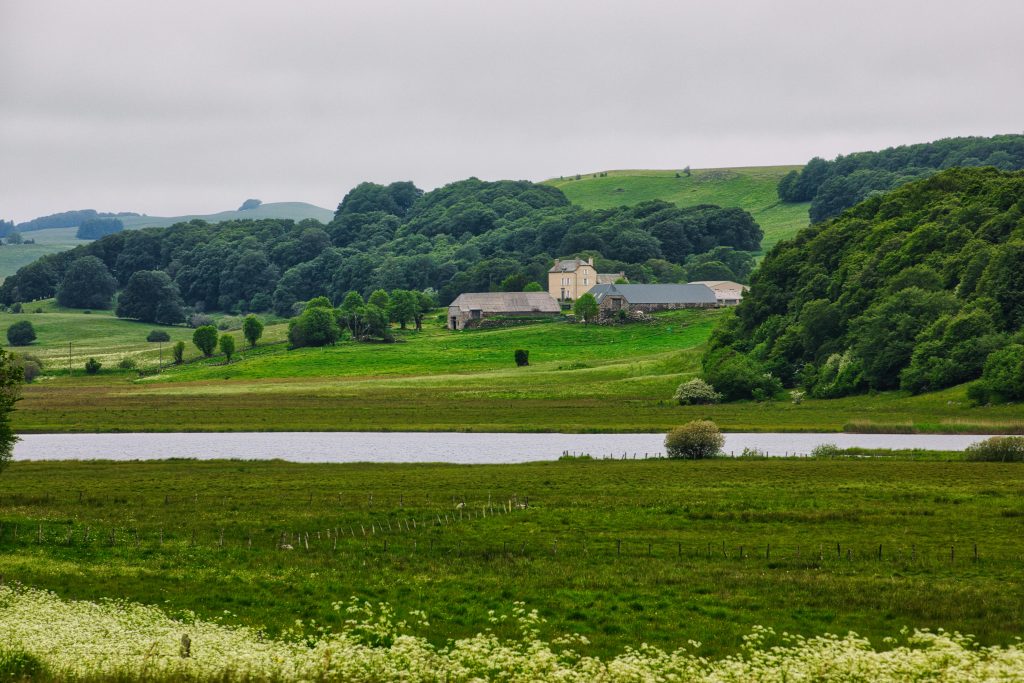 Peaceful rural landscape in France featuring a farmhouse, rolling hills, and a river.