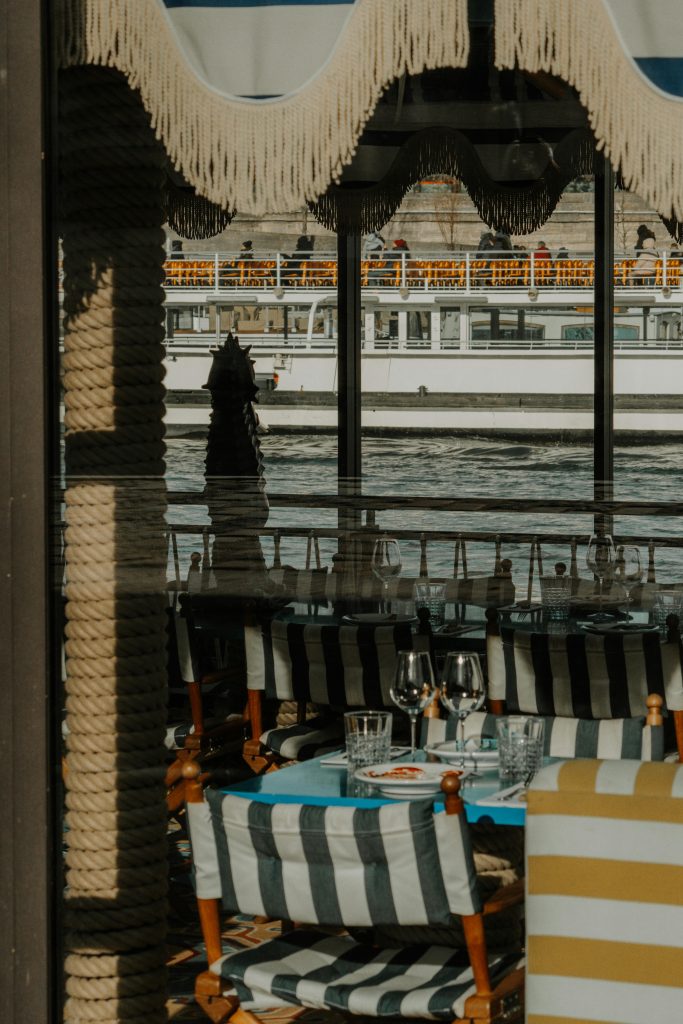 Elegant cafe interior with nautical decor in Paris, offering a serene view of the Seine river.