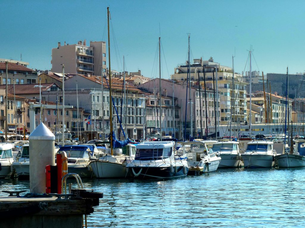 White motorized yachts moored in harbor on water surface of coastal city with residential buildings against blue sky in sunny day