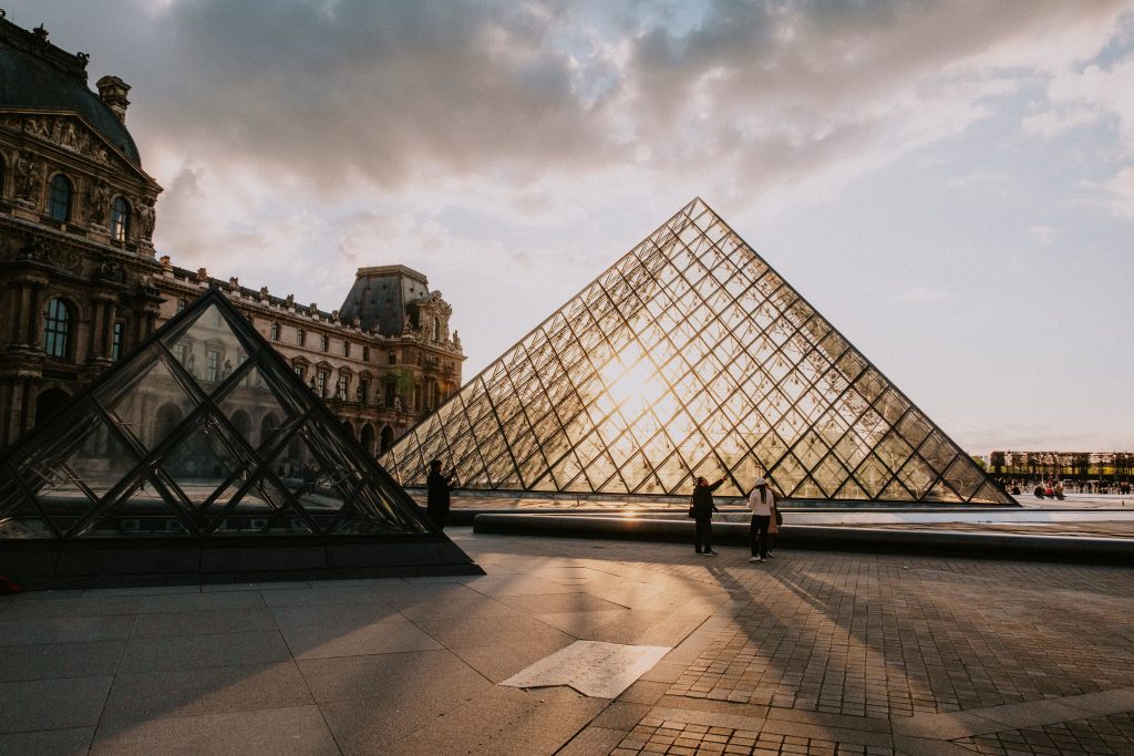 The iconic Louvre Pyramid glows with the sunset in the backdrop of Paris, France.