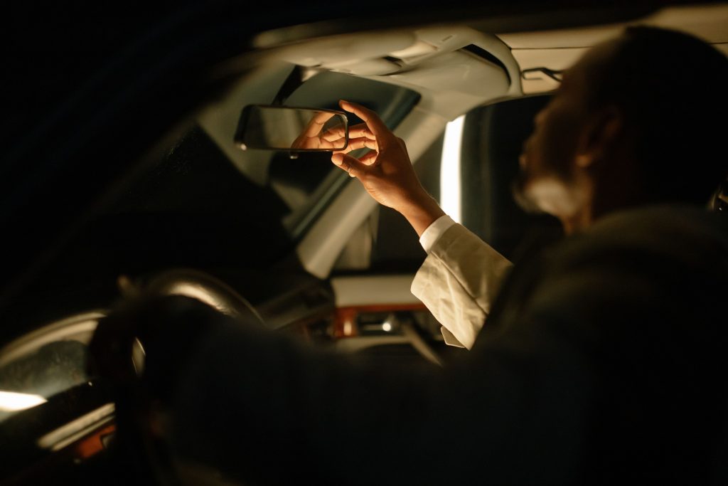 A man adjusting the rear view mirror inside a car, captured during nighttime with soft lighting.